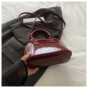 Detail view of burgundy patent leather shell bag with gold hardware and top handle