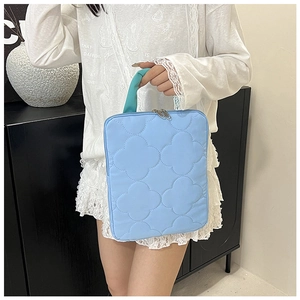 Detailed view of light blue quilted laptop sleeve with clover stitching and green handles