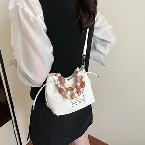 Minimalist beige drawstring bucket bag featuring a beaded handle and long shoulder strap