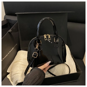 Detail of glossy black shell dome bag with gold hardware and luxury gift packaging