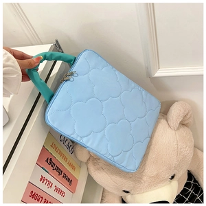 Detail of light blue quilted laptop bag with floral stitching and green handles