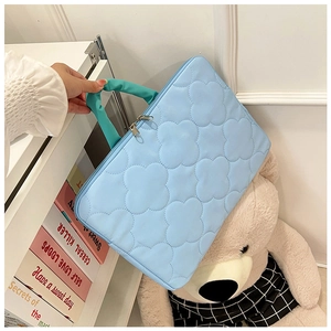 Detail of sky blue quilted laptop sleeve with flower patterns and green handles