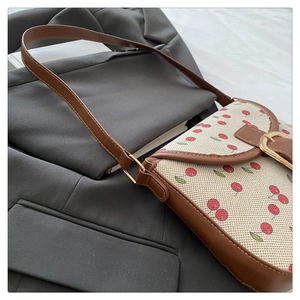 Detailed view of canvas fabric with red cherry print and brown leather trim on shoulder bag