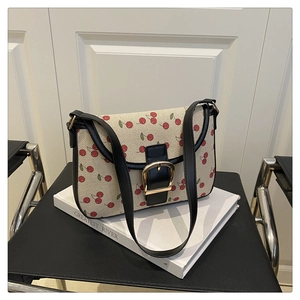 Close-up of canvas shoulder bag with cherry print, black leather trim, and gold buckle