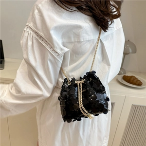 Detail of black sequin bucket bag featuring a gold chain and elegant pearl drawstring