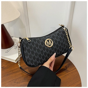 Detail of black monogram shoulder bag with gold M logo and chain strap in daily setting