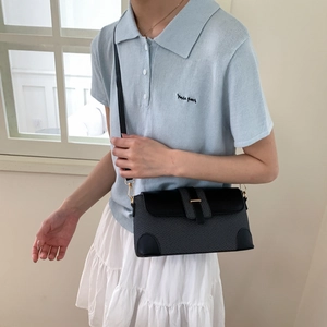 Détail du sac bandoulière tissé noir avec fermoir doré porté sur un polo bleu clair