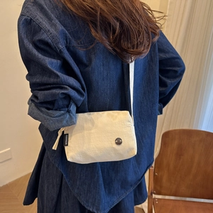 Dettaglio mini borsa a tracolla bianco crema con logo in metallo e tira-zip in tessuto