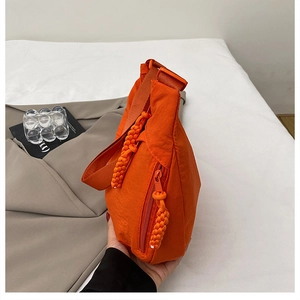 Macro shot of orange nylon crossbody bag with textured fabric and woven zipper detail