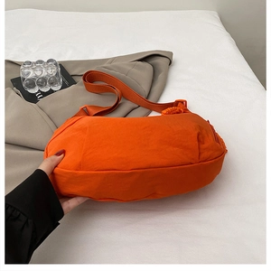 Detail view of bright orange nylon crossbody bag with side zipper and woven shoulder strap