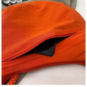 Detail of bright orange nylon crossbody bag showing the side zipper pocket and phone storage