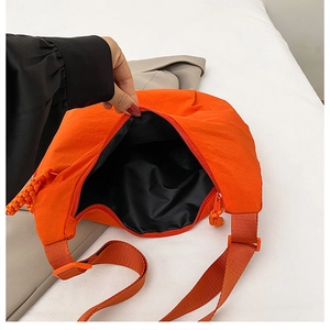 Macro detail of the bright orange crossbody bag showing black lining and zip closure