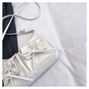 Close-up of white PU leather shoulder bag featuring bow details and multiple flap pockets