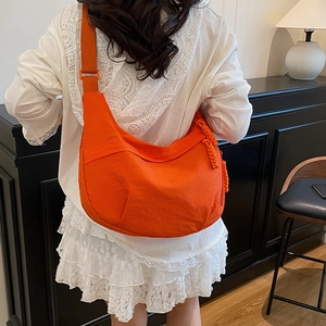 Minimalist bright orange crescent crossbody bag with woven knot detail shown on shoulder
