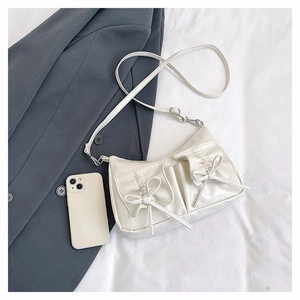 Detail of white leather shoulder bag with decorative bows and adjustable strap