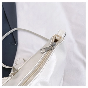 Close-up of the silver zipper and premium grain leather texture on a white shoulder bag