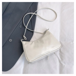 Flat lay of a white faux leather baguette bag with a slim strap and metal zipper detail