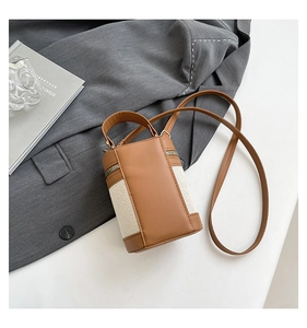 Detail of color-block cylinder bucket bag with canvas stitching and brown leather handles
