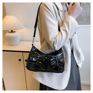 Detail of black patent leather shoulder bag with decorative bows and glossy finish