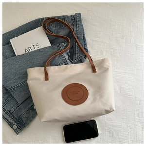 Overhead shot of a cream tote bag with brown straps and fashion patch on a casual background
