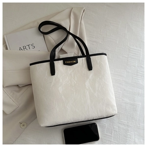 Detailed macro of the white textured tote bag featuring a black FASHION logo label