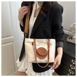 Detail of cream tote bag with brown straps and circular logo patch shown on model