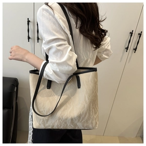 Detail of minimalist cream tote bag showing crinkled texture and black contrast piping