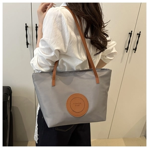 Detail of grey nylon tote bag with brown faux leather strap and circular fashion patch