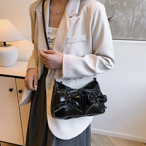 Glossy black crossbody bag with ribbon bows shown on a model in a warm room