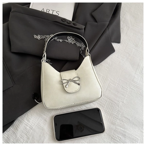Top view of cream handbag with silver bow detail, chain strap and elegant props