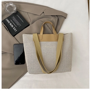 Detalle de un bolso tote tejido en blanco roto con asas de cuero camel y correa ancha