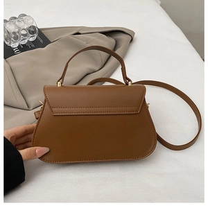 Detail view of a vintage brown trapezoid handbag with gold hardware and a top handle