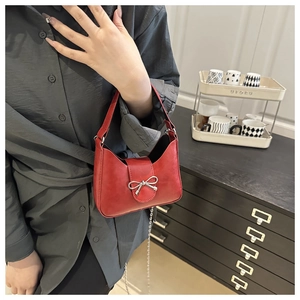 Detailed view of red leather shoulder bag with a silver metal bow accent and chain strap