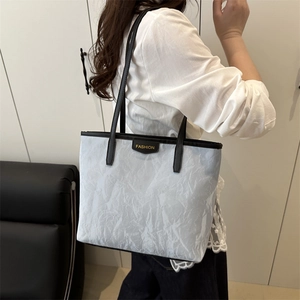Light gray pleated tote bag with black handles and fashion tag in a lifestyle setting