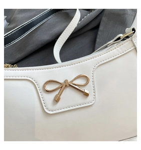 Détail d'un sac d'épaule blanc en similicuir avec un nœud doré et une fermeture éclair