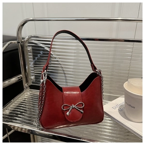Macro detail of wine red leather handbag with silver metallic bow and chain strap