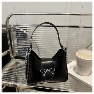 Detail of black glossy handbag with silver bow accent and leather chain strap on glass shelf