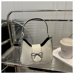 Detail of elegant cream shoulder bag with metallic bow and detachable silver chain strap