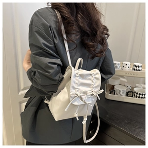 Detail view of white PU leather mini backpack featuring elegant bow ties and pleated flap