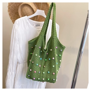Detail of green knit tote bag with colorful beads on a hanger with summer hat and dress