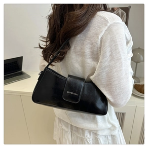 Close-up of black glossy shoulder bag showing premium texture and branded flap design