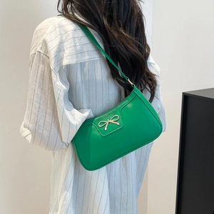 Sac baguette en cuir vert avec nœud doré porté à l'épaule par un mannequin