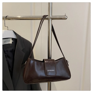 Detail of a shiny dark brown baguette bag with adjustable strap in a city style setting