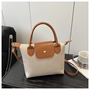 Detail of beige and brown tote bag with woven texture and gold snap on wood desk