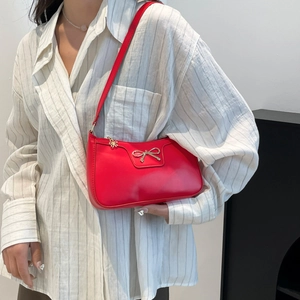 Détail d'un sac à bandoulière rouge avec nœud doré et pendentif fleur de fermeture