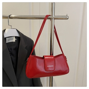 Detail of red patent leather baguette bag featuring a brand logo on the front flap