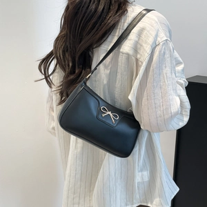 Détail du sac porté épaule noir avec boucle nœud argentée sur chemise à rayures blanches