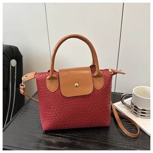 Detail view of red woven texture handbag with brown leather handles and flap closure