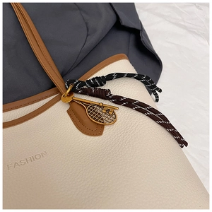 Close-up of beige lychee grain tote bag with gold tennis racket charm and fashion logo