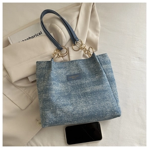 Detail of blue denim tote bag with gold chain strap and stylish silver glitter accents